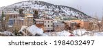 Colorful houses and buildings on a snow-covered hill at Park City in Utah. There are different types of buildings and houses on a hill that are covered in snow with a mountain view at the back.