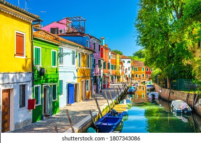 Colorful houses of Burano island. Multicolored buildings on fondamenta embankment of narrow water canal with fishing boats in sunny day, Venice Province, Veneto Region, Northern Italy. Burano postcard