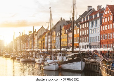 Colorful houses in Copenhagen old town at sunset, with boats and ships in the canal in front of them.