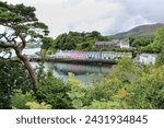 Colorful houses located in the bustling Portree Harbour, viewpoint between foreground trees. 