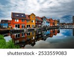 Colorful houses reflecting in the water of a canal in Groningen, Netherlands under a cloudy sky.