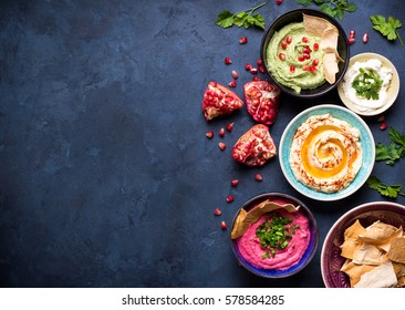 Colorful hummus bowls background. Different kinds of dips. Traditional hummus, herbs hummus, beetroot hummus, spread. Assorted meze and dips with crispy pita. Space for text. Meze and snacks concept