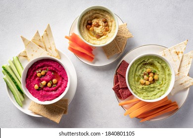 colorful hummus in bowls, served with vegetables sticks and crackers. Traditional hummus, beetroot hummus and avocado hummus. Meze and healthy snacks concept. top view. - Powered by Shutterstock