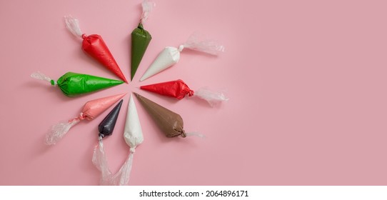 Colorful icing bags to cover Christmas gingerbread, cakes and cookies on a pink background.  Set for decorating desserts. New Year's colors. Cake decorating tools. Confectionery Banner concept.