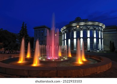 Colorful illuminated fountain display in front of a neoclassical building with columns at night. The scene captures the vibrant nightlife and architecture of Cherkasy, Ukraine - Powered by Shutterstock