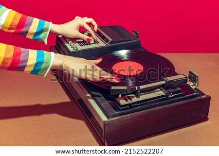 Colorful image of female hands spinning retro vinyl record player like a dj isolated over red background. Bright design with vintage things. Concept of pop art, fashion, music, mix old and modernity