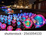 Colorful inflatable spheres glowing blue and pink on water during a nighttime street event in Liverpool