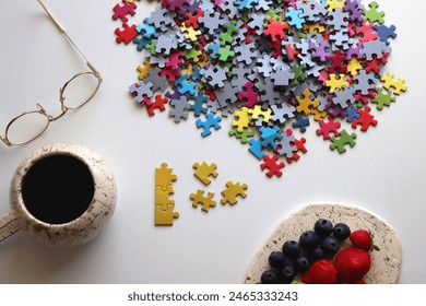 Colorful jigsaw puzzle pieces, cup of tea or coffee, eyeglasses and fresh berries for snacking. Hygge at home. Selective focus. - Powered by Shutterstock