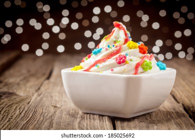 Colorful Kids Ice Cream Party Dessert With A Twirl Of Rich Creamy Vanilla Ice Cream Topped With Vibrant Candy And Sprinkles Decorated With Orange Syrup With A Bokeh Of Sparkling Festive Lights