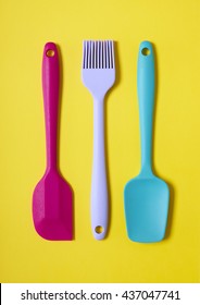 Colorful Kitchen Cooking Utensils - A Pink And Blue Baking Spatula, And A Purple Pastry Brush On A Yellow Background