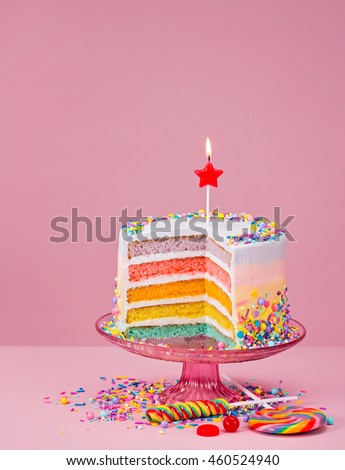 Colorful layered Birthday cake with sprinkles over a pink background.