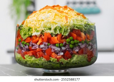 Colorful layered salad displayed in a glass bowl with fresh vegetables and cheese on a kitchen counter - Powered by Shutterstock