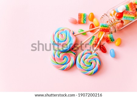 Colorful lollipops swirls on sticks in glass bottle. Striped spiral multicolored candy on pink background, top view