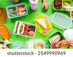 Colorful lunchboxes with sandwiches, fruits, and snacks on a green table. Kids