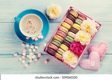 Colorful macaroons, coffee and marshmallow on wooden table. Sweet macarons in gift box and hearts. Top view. Retro toned - Powered by Shutterstock