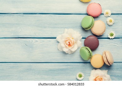 Colorful macaroons and flowers on wooden table. Sweet macarons. Top view with copy space for your text. Retro toned
