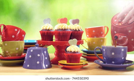 Colorful Mad Hatter Style Tea Party With Cupcakes And Rainbow Colored Polka Dot Cups And Saucers, With Bokeh Garden Background And Lens Flare, Pouring Tea. 