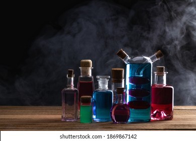Colorful magic potion bottles on wooden table. Medieval alchemist laboratory with various kind of flasks. Esoteric, gothic and occult background.