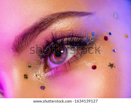 Colorful makeup. Bright and intense makeup. Female eye close-up with bright makeup. Fashionable stylish makeup with the use of sequins. Stylish image. The face is illuminated by bright lights.