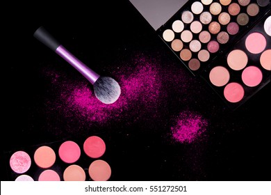 Colorful makeup palette and pink big brush to apply powder on pure black background. Professional makeup equipment.