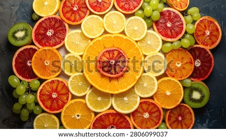 A colorful mandala pattern created with sliced citrus fruits like oranges, blood oranges, lemons, and kiwis, interspersed with green grapes.