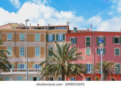 Colorful Mediterranean buildings with green shutters under a clear blue sky in Menton. Palm trees and modern streetlamps enhance the vibrant urban scene, capturing the essence of Mediterranean charm. - Powered by Shutterstock