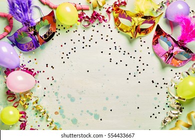 Colorful Metallic Foil Carnival Masks And Party Balloons Forming A Frame Around Central Light Green Copy Space With Streamers And Confetti