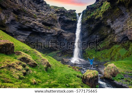 Colorful morning view of Kvernufoss waterfall with man standing on the rock. Majestic sunrise in south Iceland, Europe. Artistic style post processed photo.