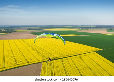 Parapente motorisée et colorée volant librement au-dessus des champs de colza jaune au printemps à horizon bleu. département d'Essonne, région Ile-de-France, France