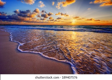 Colorful ocean beach sunrise with deep blue sky and sun rays