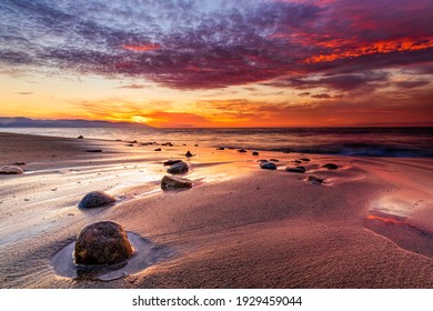 A Colorful Ocean Sunset With Rocks On The Beach And A Vibrant Cloudscape Overhead In The Sunset Sky