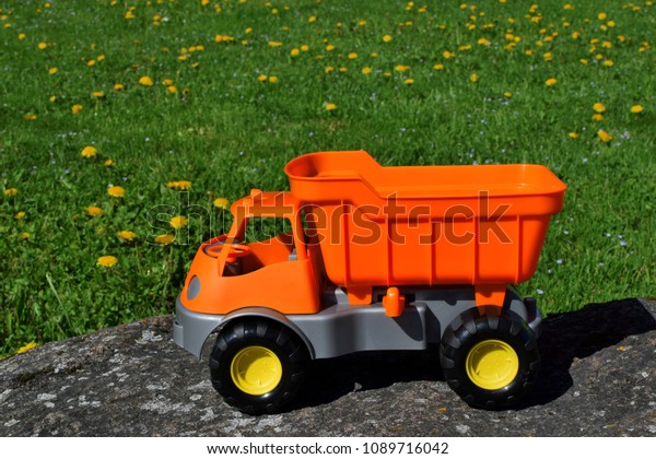 Colorful orange toy car on natural big stone on\
green meadow grass background in sunny summer day with copy space\
for text.\
