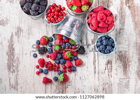 Colorful overhead fresh berries assorted arrangement  in six tin metallic cans and spilled mixed fruit on rustic white wooden table in studio. Blueberry, raspberry, red currant, strawberry, blackberry
