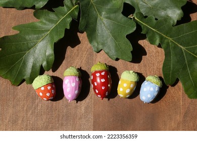 Colorful Painted Acorns With Polka Dot Pattern And Green Oak Leaves On Wooden Table, Flat Lay