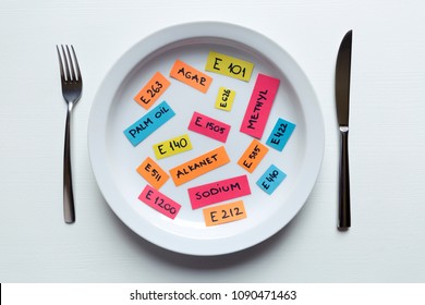 Colorful paper notes naming food additives on plate with fork and knife, food additive and unhealthy food concept. - Shutterstock ID 1090471463