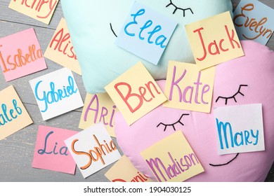 Colorful paper sheets with written different baby names on grey wooden table, flat lay