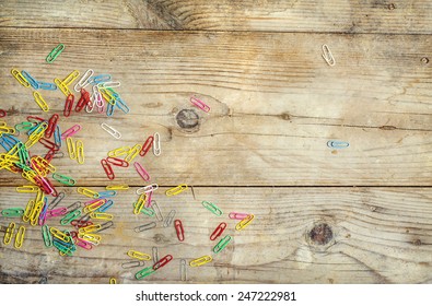 Colorful Paperclips Scattered On Wooden Floor Background. View From Above.