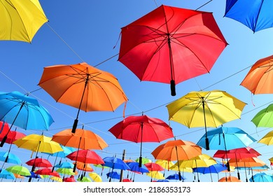 Colorful Parasol Sun Protection. Bright Umbrellas Suspended Overhead On Metal Wires. Climate Change And Global Warming Concept. Summer Travel Tourism And Vacation Theme. Design And Urban Environment.