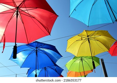 Colorful Parasol Sun Protection. Bright Umbrellas Suspended Overhead On Metal Wires. Climate Change And Global Warming Concept. Summer Travel Tourism And Vacation Theme. Design And Urban Environment.