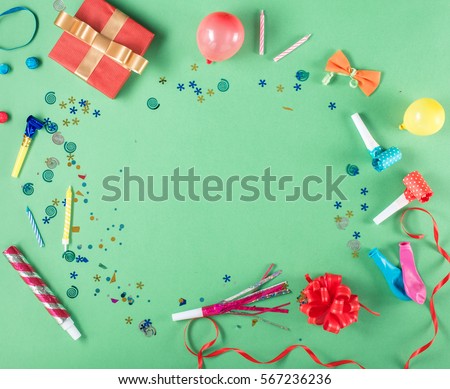 Colorful party frame with red gift box with various party confetti, balloons, streamers, noisemakers and decoration on a green background. Colorful celebration background. Flat lay.