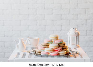 Colorful pastel pink, yellow, beige and brown french macaroons. Macarons on steel tray with tea set on white wooden table on the background of white brick wall. - Powered by Shutterstock