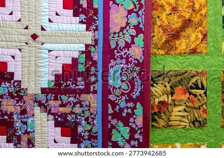 Colorful patchwork quilt features vibrant floral and autumn leaf patterns in rich purples, greens, and yellows, handmade craft, cozy home decor, textile art.