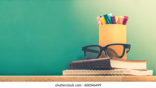 Colorful Pen In Box With Black Eyeglasses On Stack Of Study Notebook On Wooden Table With Blackboard Wall,Mock Up Template Banner For Adding Text Or Design,education Concept,vintage Filter