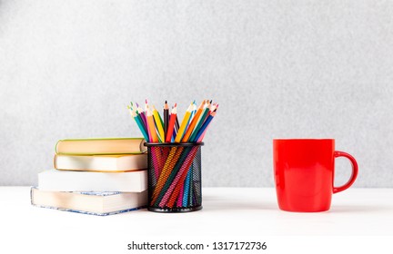 colorful pencils, books and red cup on a desk with gray background and copyspace - Powered by Shutterstock