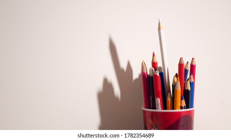 Colorful Pencils In Red Glass On A White Background With Stark Shadows.