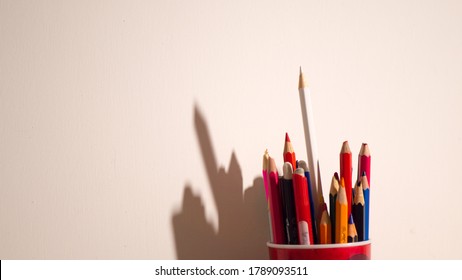 Colorful Pencils In Red Glass On A White Background With Stark Shadows.