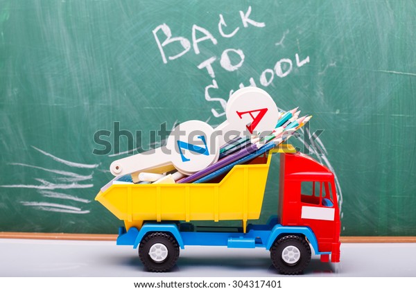 Colorful pencils of red yellow orange violet purple
pink green blue chalk and fan english alphabet in plastic truck car
toy lying on white school desk on back to school text, horizontal
photo