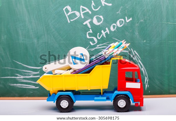 Colorful pencils of red yellow orange violet purple
pink green blue chalk and fan english alphabet in plastic truck car
toy lying on white school desk on back to school text, horizontal
photo