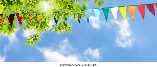 colorful pennant string decoration in green tree foliage on blue sky, summer party background template banner with copy space - Shutterstock ID 2282824125