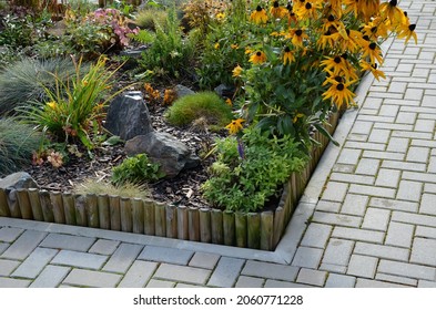 A Colorful Perennial Flowerbed At The Entrance To The Garden Bordered By A Decorative Wooden Palisade. From The Back It Is Connected By A Wire. Flowers And Stones Bloom In The Autumn Sun.